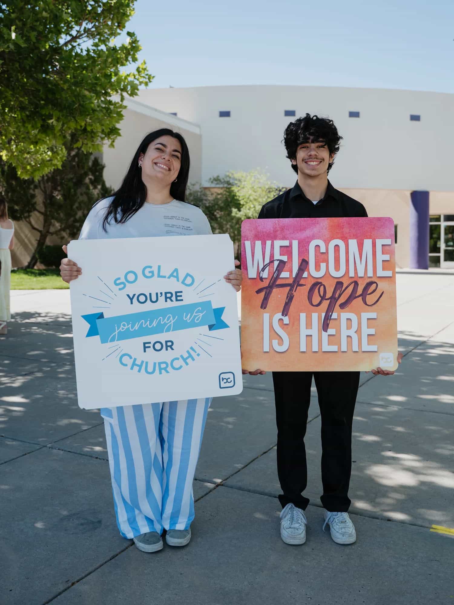Two host team members holding welcome signs outside Believer Church