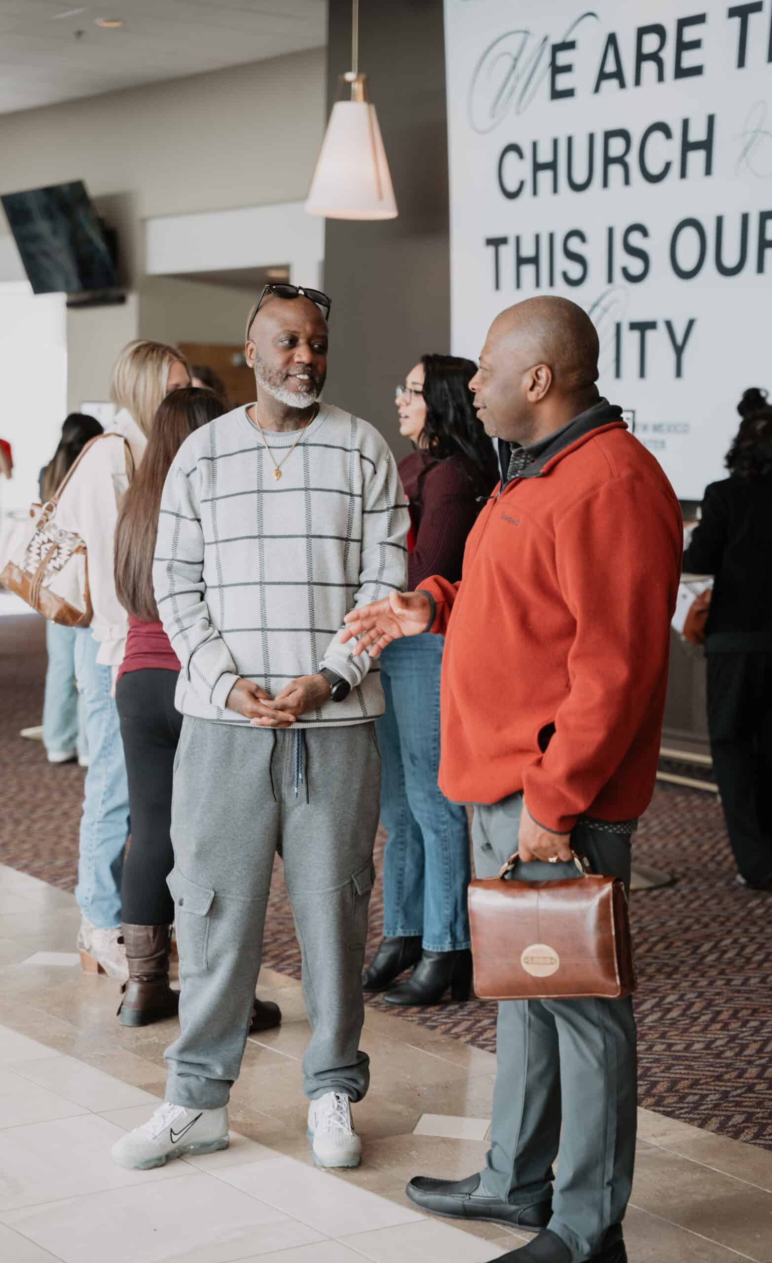 Two men talking in a church lobby, one holding a Bible case