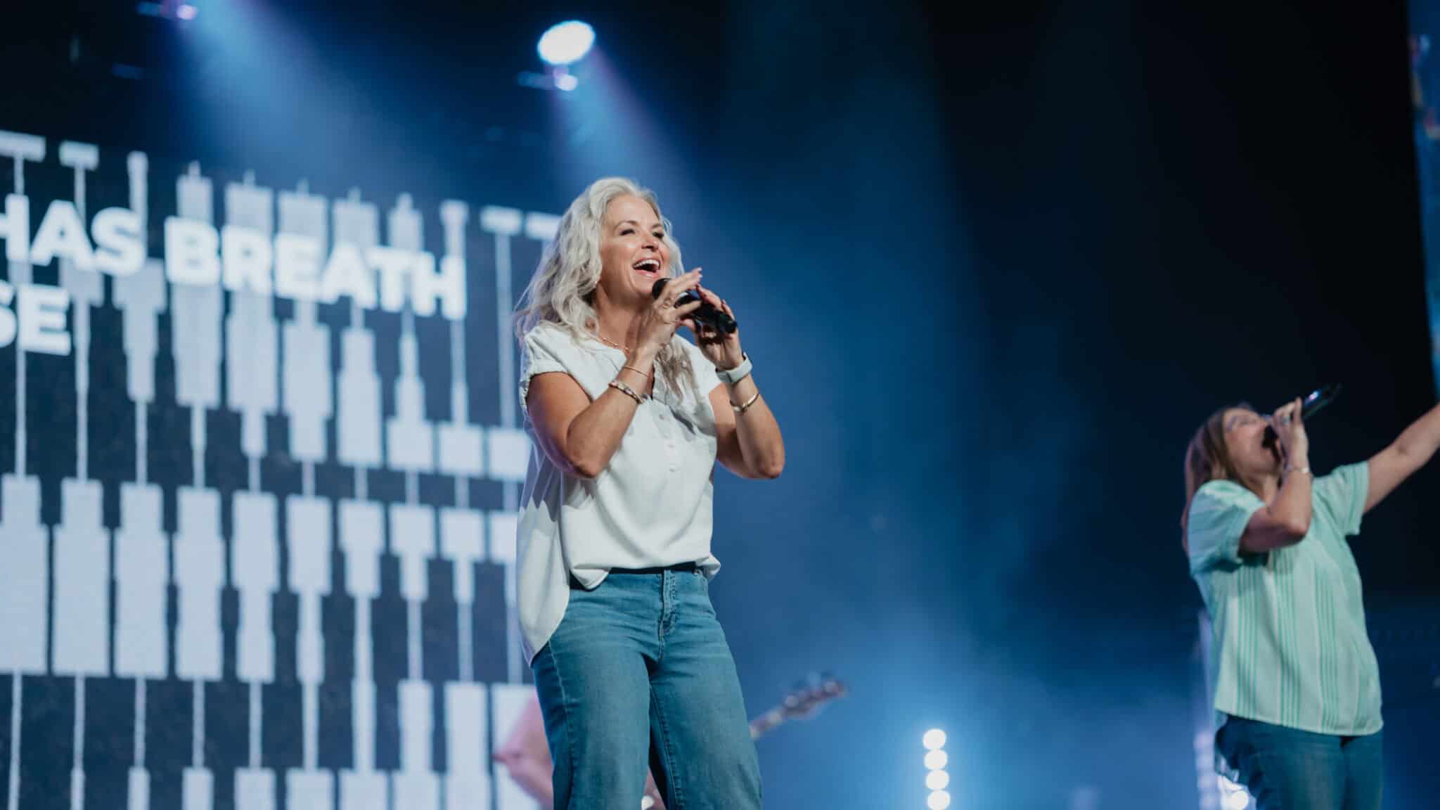 Woman singing into a microphone during worship on stage
