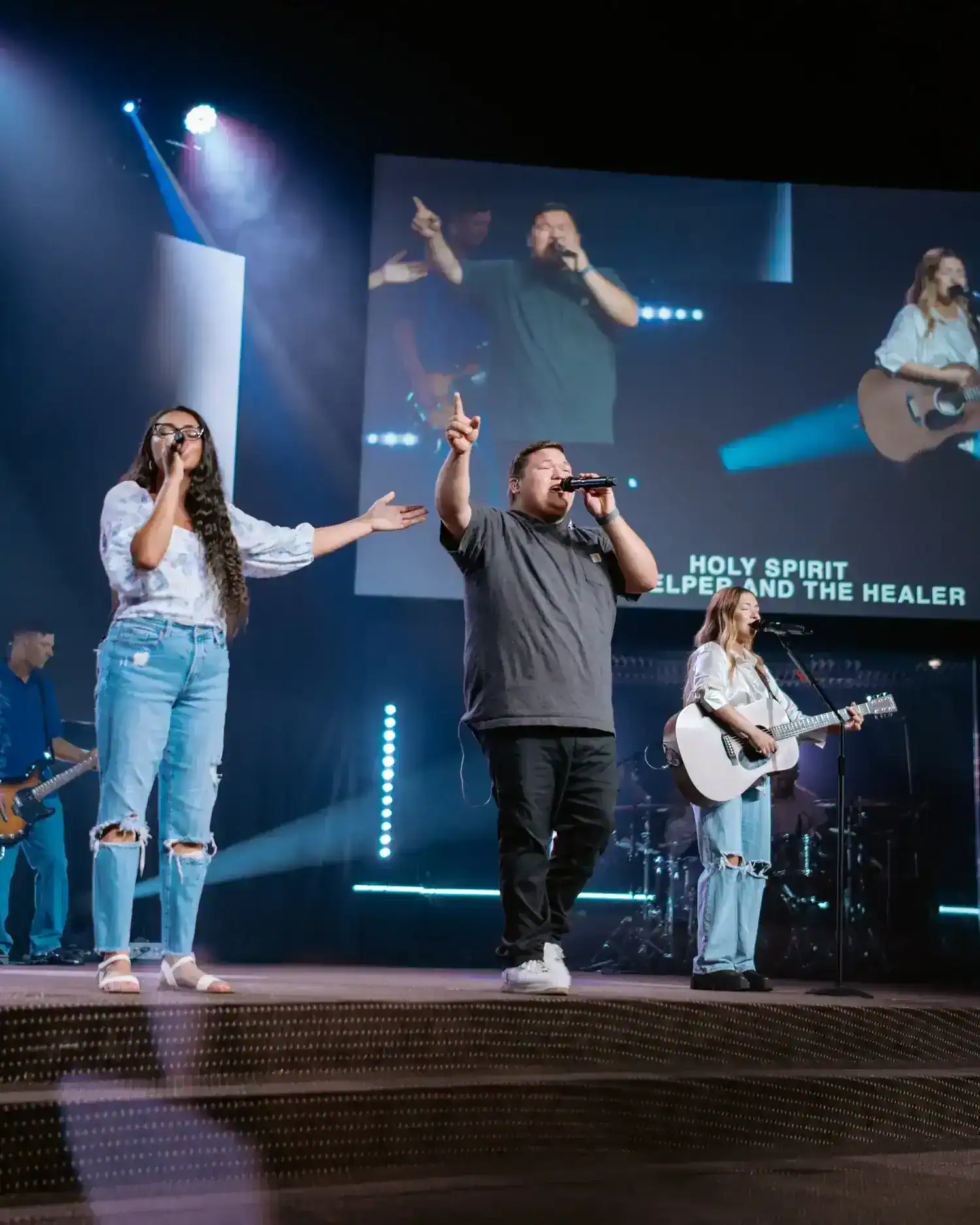 Worship team singing on stage with hands raised under stage lights